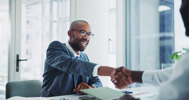 Two people shaking hands across a desk during a business onboarding meeting.